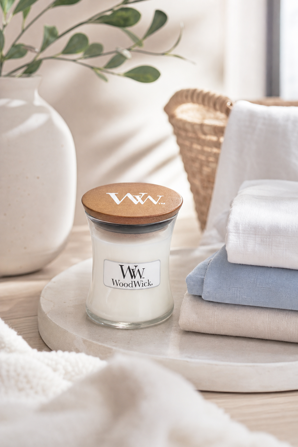 WoodWick Kerze mit Deckel neben gefalteten Textilien und Vase