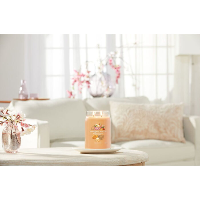 Brennende Mango Ice Cream Duftkerze neben Blumen auf einem Glastisch