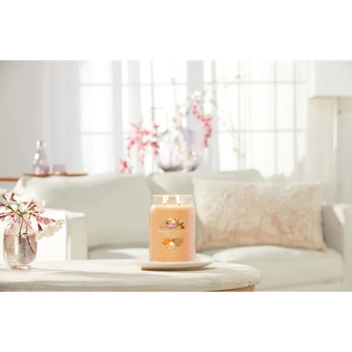 Brennende Mango Ice Cream Duftkerze neben Blumen auf einem Glastisch