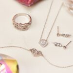 Herzarmband neben Ring, Halskette und Ohrringen mit glänzenden Schmucksteinen