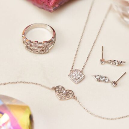 Herzarmband neben Ring, Halskette und Ohrringen mit glänzenden Schmucksteinen