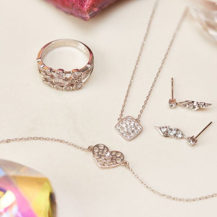 Herzarmband neben Ring, Halskette und Ohrringen mit glänzenden Schmucksteinen