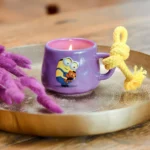 Brennende lila Minions-Kerze mit Kordel auf dekorierter Tischplatte