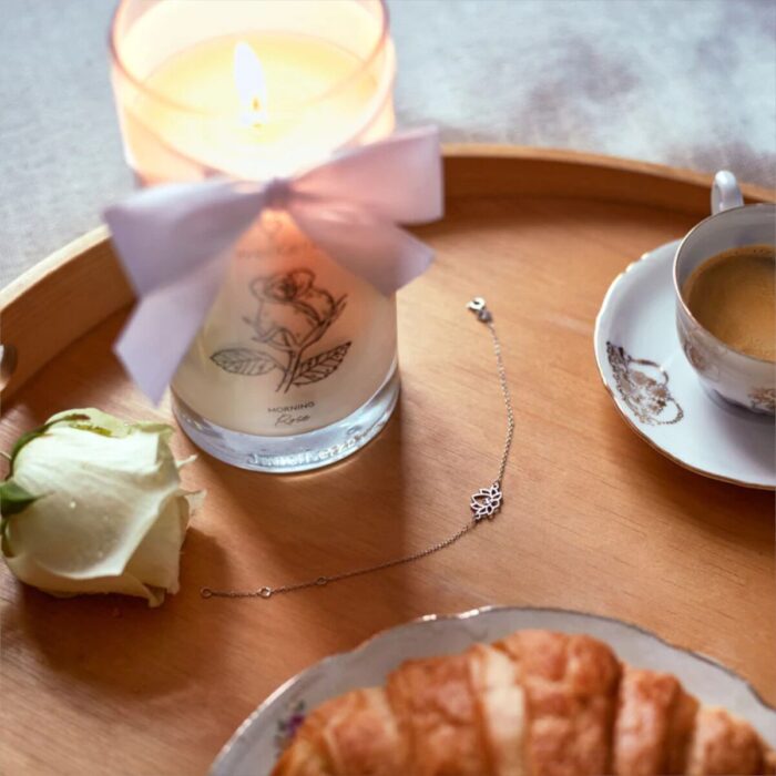 Brennende Morning Rose Kerze neben einem filigranen Armband und einer Kaffeetasse