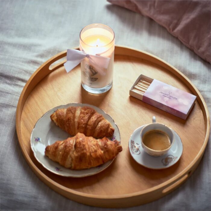Brennende Morning Rose Kerze auf Tablett mit Croissants und Kaffeetasse