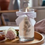 Brennende JewelCandle Morning Rose Kerze mit weißer Schleife neben einer Rose