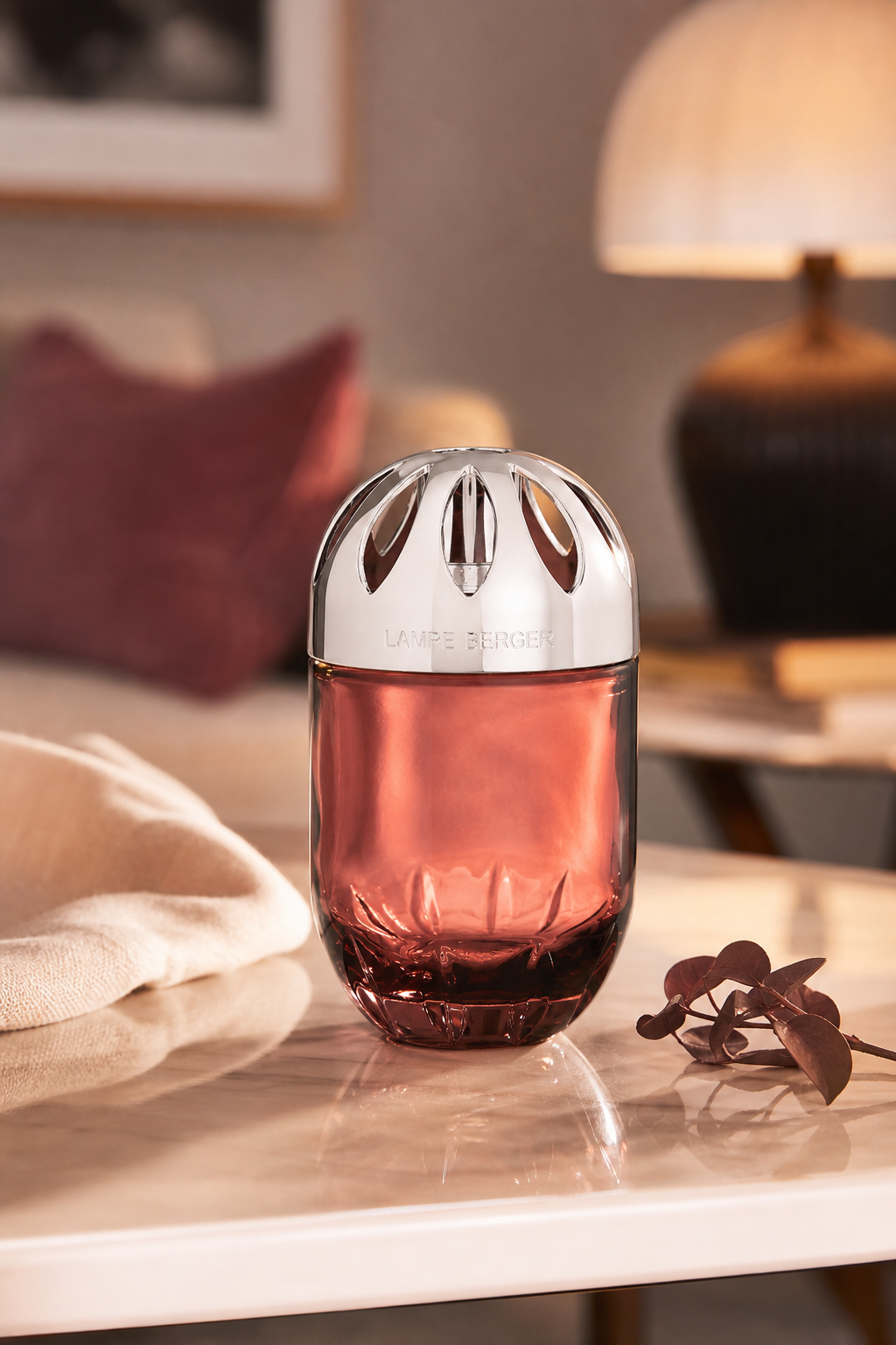 Pflaumenfarbene Lampe Berger steht auf einem Tisch neben dekorativen Zweigen