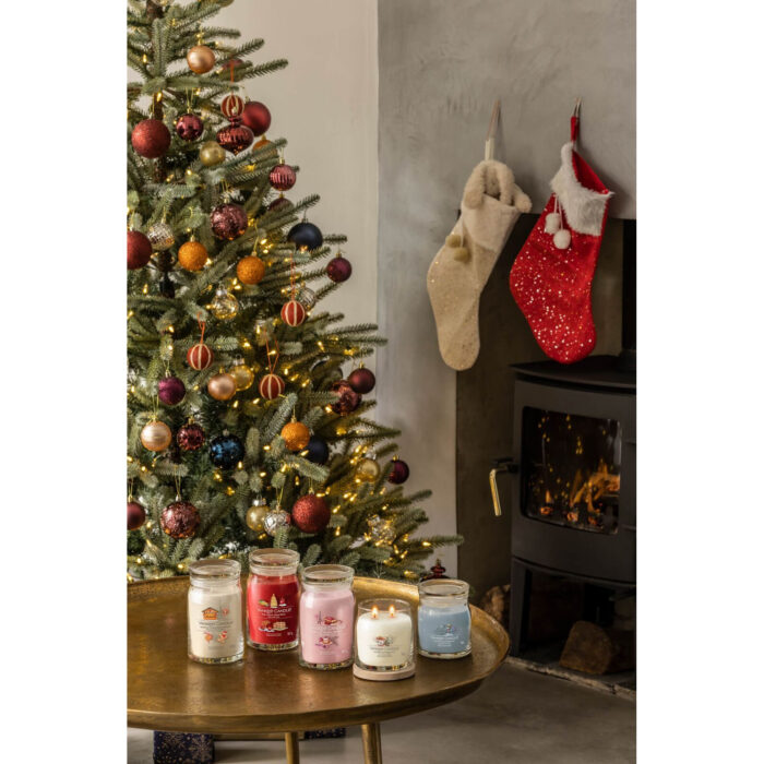 Mehrere Yankee Candle Gläser stehen vor beleuchtetem Weihnachtsbaum und Kamin