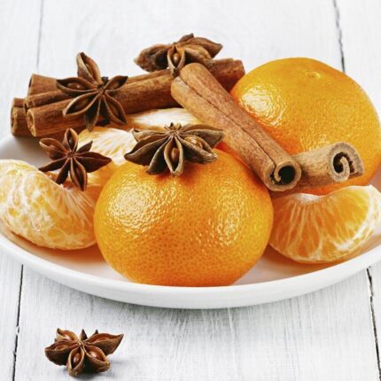 Brennende Orange-Cinnamon-Kerze mit geöffnetem Glasdeckel auf einem Tisch