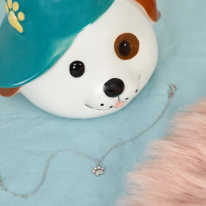 Silberfarbenes Armband mit Pfotenanhänger neben einer Hundfigur