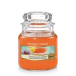 Orangefarbene Duftkerze im Glas mit transparentem Deckel und Passion-Fruit-Martini-Etikett