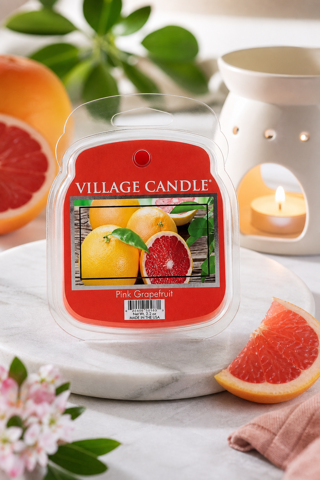 Village Candle Pink Grapefruit Duftwachs neben beleuchteter Aromalampe und Grapefruits