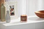 Brennende Yankee Candle Praline & Birch Kerze neben Vasen und Bilderrahmen