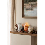 Drei Yankee Candle Gläser auf einem Wandregal, mittlere orange Kerze mit zwei Flammen