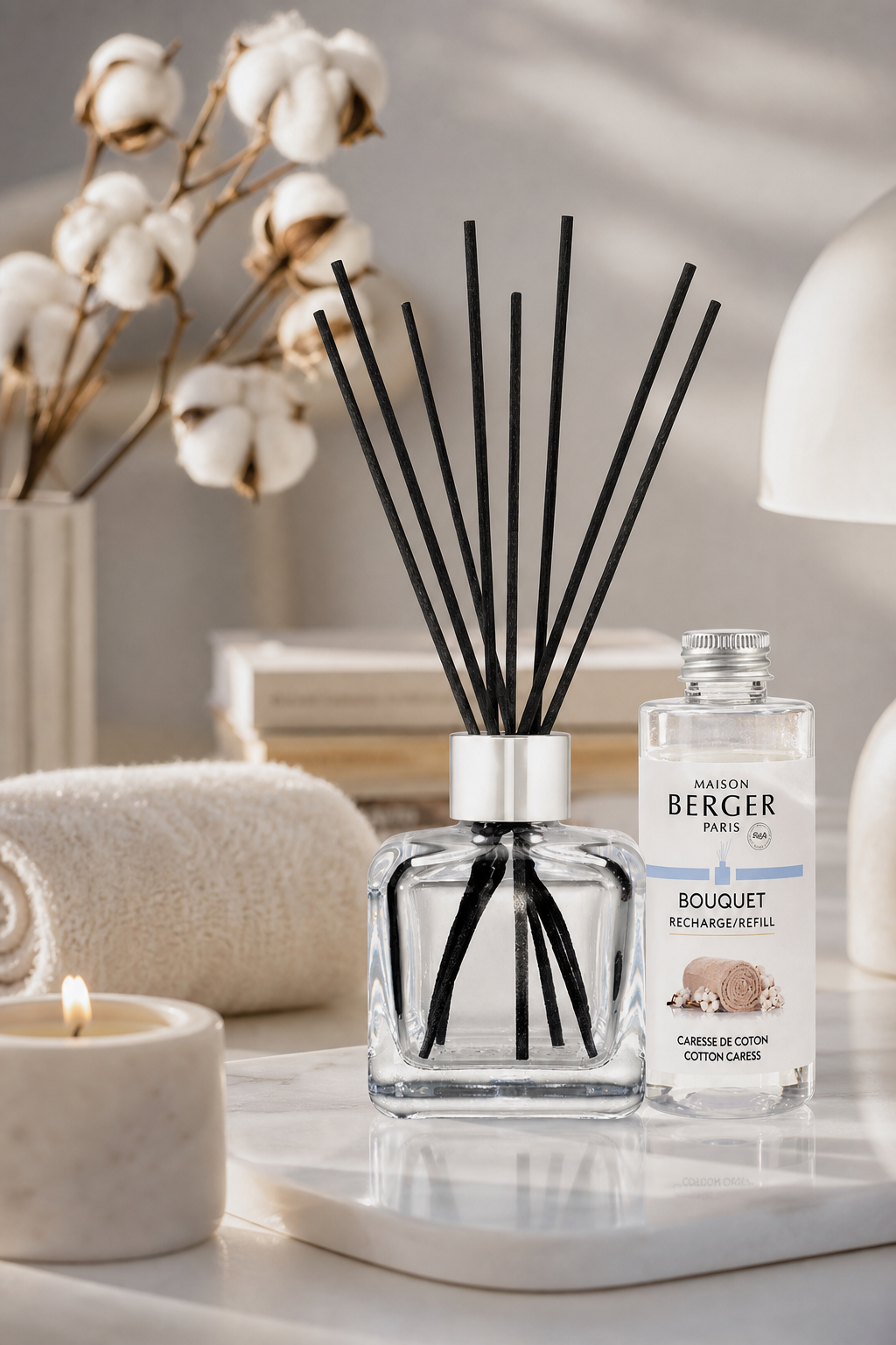 Raumduft-Diffuser mit schwarzen Stäbchen und Nachfüllflasche neben Baumwollzweigen