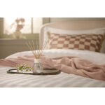 Reed Diffuser mit Duftstäbchen auf einem Tablett vor einem Bett