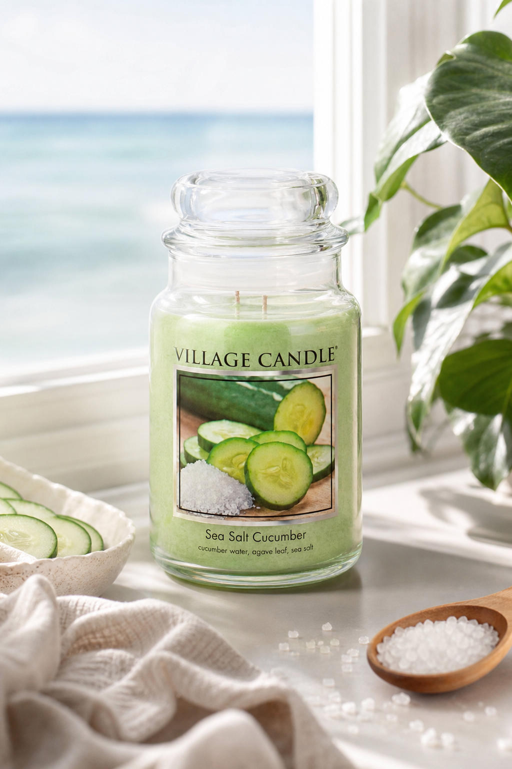 Grüne Village Candle im Glas vor Fenster mit Meerblick und Pflanze