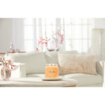 Brennende Mango Ice Cream Duftkerze vor Sofa und Blumen