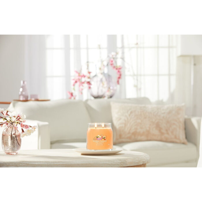 Brennende Mango Ice Cream Duftkerze vor Sofa und Blumen