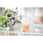 Brennende Mango Ice Cream Duftkerze auf einem Glastisch neben Blumen