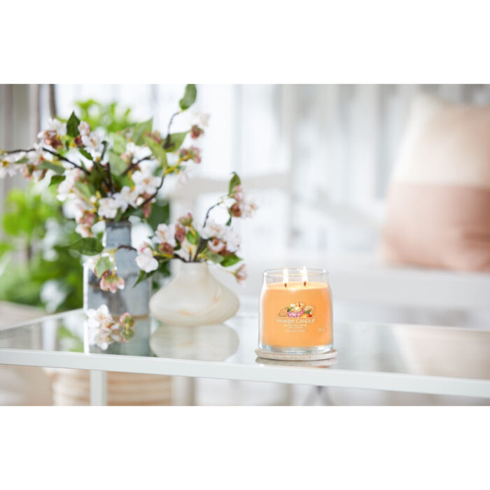 Brennende Mango Ice Cream Duftkerze auf einem Glastisch neben Blumen