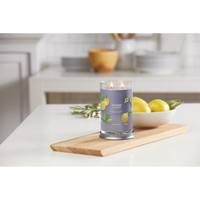 Brennende Black Tea & Lemon Kerze auf Holztablett mit Zitronen im Hintergrund