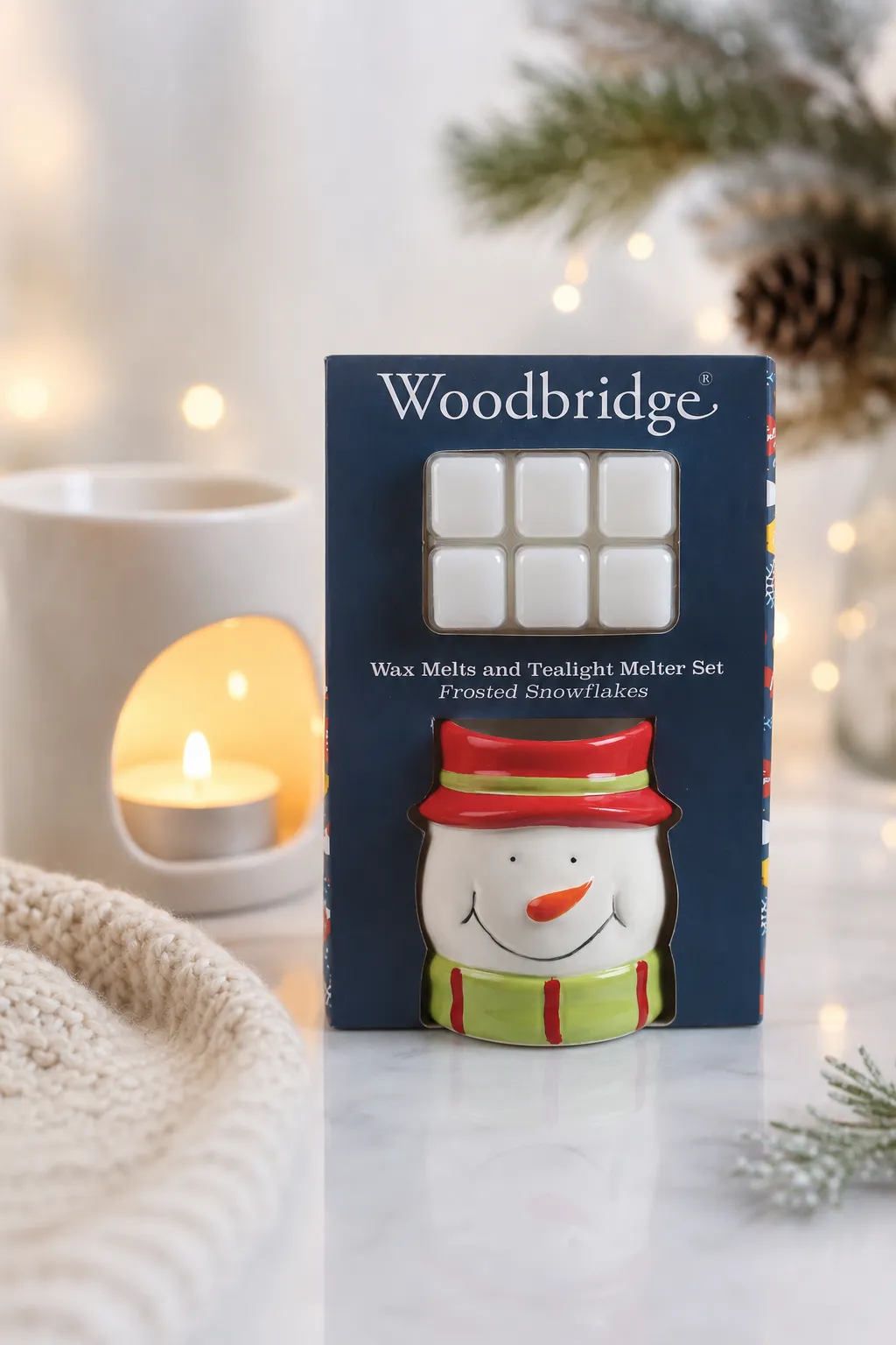 Verpacktes Schneemann-Wachsset Woodbridge Verpackung mit Schneemann-Duftlampe und sechs weißen Wachsmelts neben einer Kerze