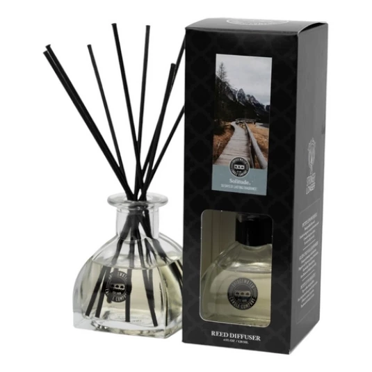 Reed Diffuser neben Verpackung Glasflakon mit schwarzen Duftstäbchen neben der Verpackung des Solitude Reed Diffusers