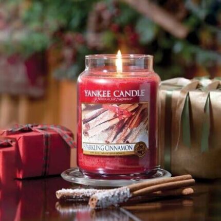 Brennende Yankee Candle Sparkling Cinnamon Kerze neben Zimtstangen und Geschenken