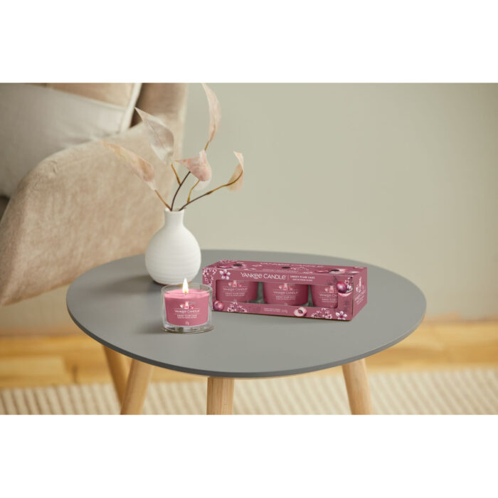 Yankee Candle Sweet Plum Sake Packung und angezündete Votivkerze auf Tisch