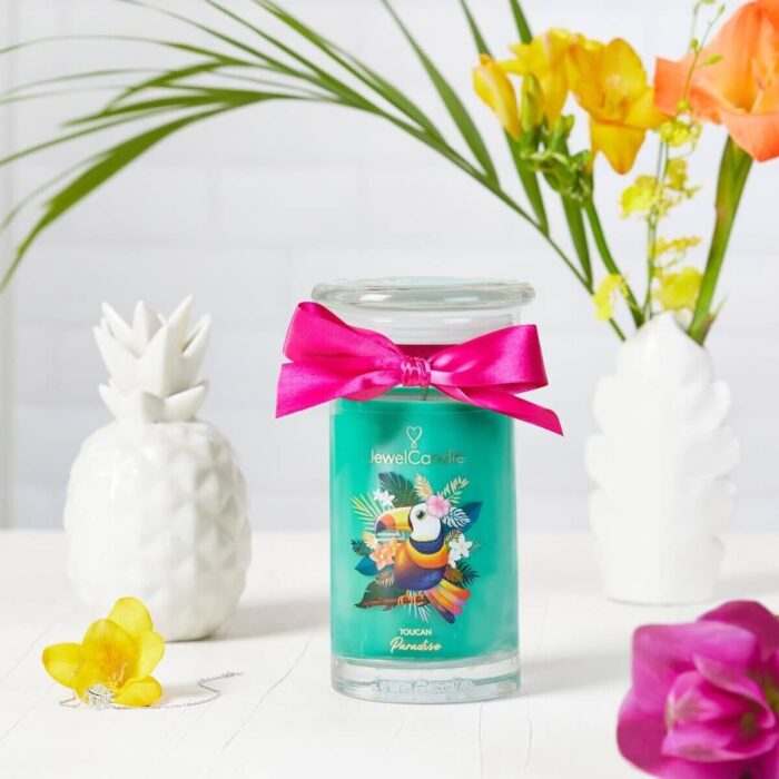 Toucan Paradise Kerze mit Tukanmotiv zwischen weißen Dekorobjekten und Blumen