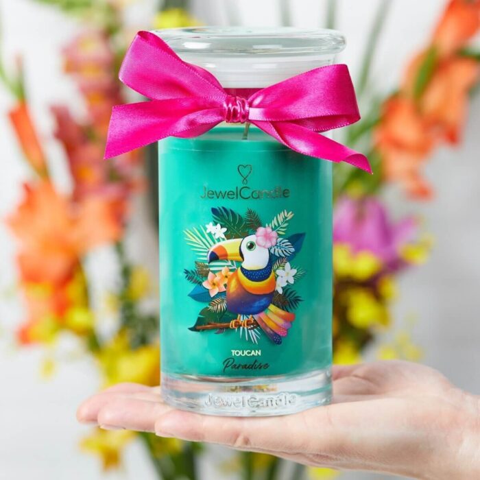 JuwelCandle Kerze mit Tukanmotiv und pinker Schleife in einer Hand