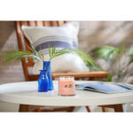 Brennende Tropical Breeze Kerze auf einem Tisch neben blauen Vasen