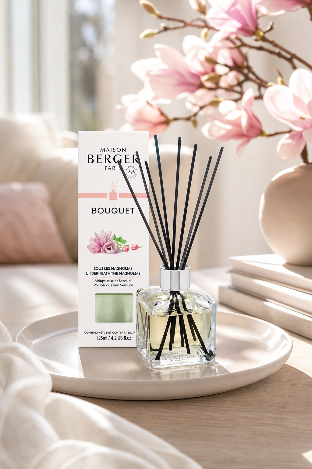 Raumduft-Diffuser mit Verpackung auf einem Tisch vor Magnolienblüten
