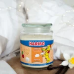 Haribo Duftkerze auf Holztisch neben Vanilleschoten und weißen Blüten
