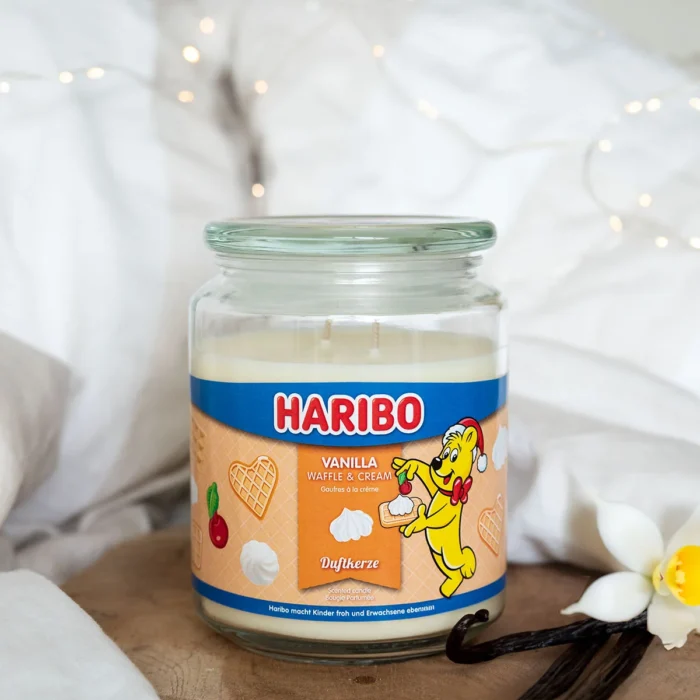 Haribo Duftkerze auf Holztisch neben Vanilleschoten und weißen Blüten
