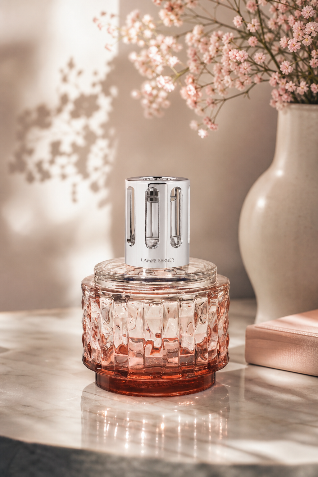 Roséfarbene Duftlampe mit silberner Kappe auf einem Tisch neben einer Vase