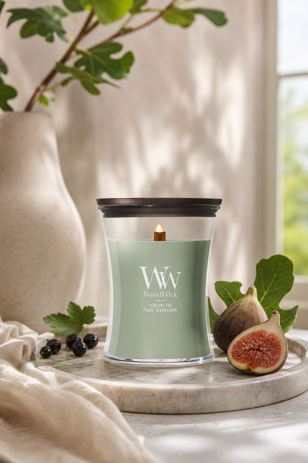 Brennende WoodWick Verdant Fig Kerze neben Feigen und Feigenzweig