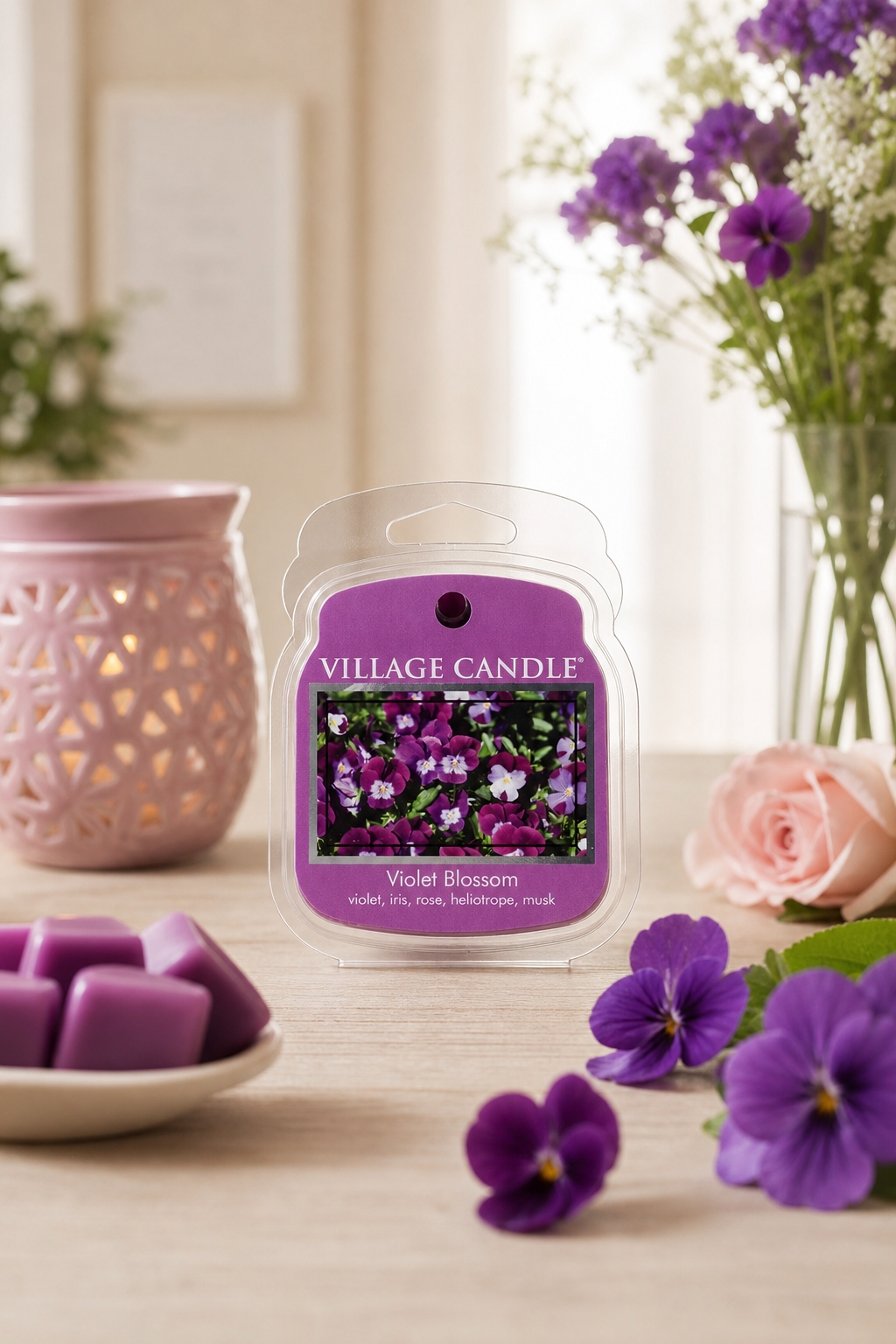 Village Candle Violet Blossom Verpackung neben Blumen und lilafarbenen Wachsformen