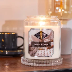 Brennende Warm & Cozy Duftkerze im Glas neben einer Tasse