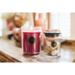 Brennende rote Welcome Home Kerze neben einem Glas mit Korken