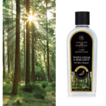 Flasche mit White Cedar & Bergamot Lamp Fragrance vor einem Nadelwald