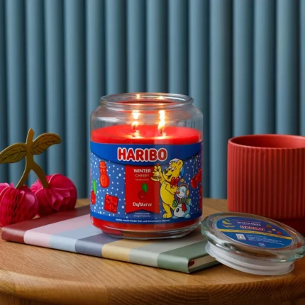 Brennende Haribo Winter Cherry Duftkerze mit zwei Flammen auf einem Tisch
