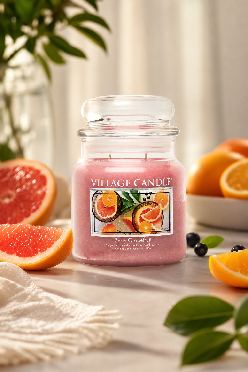 Zesty Grapefruit Kerze von Village Candle zwischen aufgeschnittenen Grapefruits